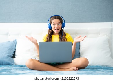 Teenager Girl In Headphones Relax On Bed At Home Using Laptop. Child In Earphones Browse Internet On Computer. Expressive Emotional Excited Teen Girl.