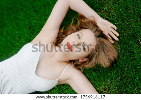 A teenager girl lies on the grass in a beautiful white dress, rests, enjoys nature. Girl with short blond hair. Beautiful and healthy skin and youth