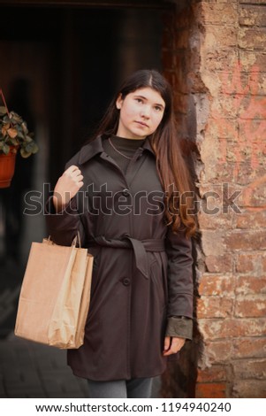 teenager girl with long brown hair street photo with shoping bag on city windowshop background