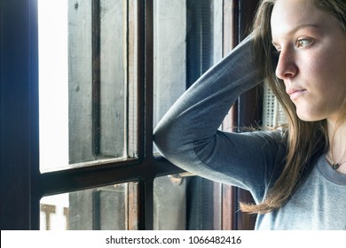 A Teenager Girl Looking Away Through A Window At Home, Thinking, Sad.