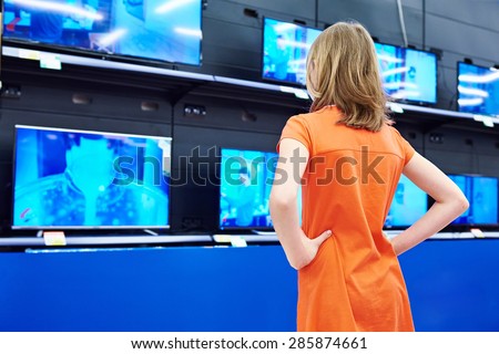 Teenager girl looks at LCD TVs in supermarket