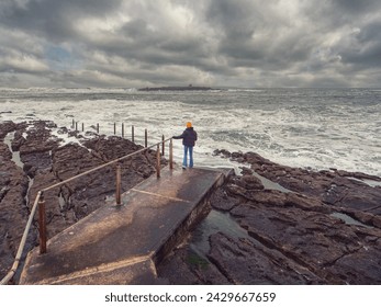 Teenager girl on foot path to the ocean by rough stone coastline of Ireland. Doolin pier area. Stunning nature scene with ocean waves, cliff and dramatic dark sky. Travel, tourism and sightseeing. - Powered by Shutterstock