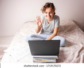 Teenager girl on quarantine is studying online on her bed. Home schooling
