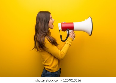 Teenager girl on vibrant yellow background shouting through a megaphone to announce something in lateral position - Shutterstock ID 1234013356