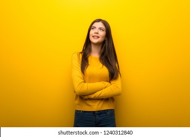 Teenager Girl On Vibrant Yellow Background Looking Up While Smiling