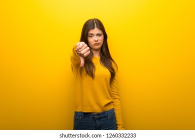 Teenager Girl On Vibrant Yellow Background Showing Thumb Down Sign With Negative Expression