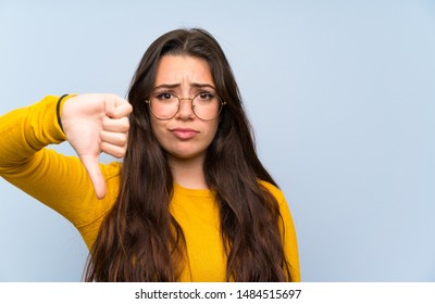 Teenager Girl Over Isolated Blue Wall Showing Thumb Down Sign