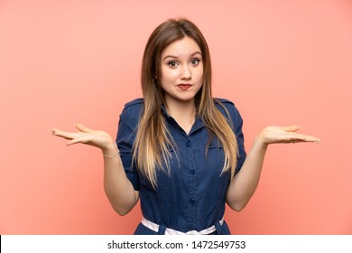Teenager girl over isolated pink background having doubts while raising hands