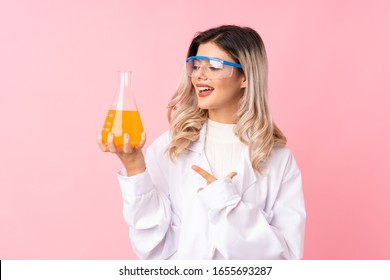 Teenager girl over isolated pink background with a scientific test tube and pointing it