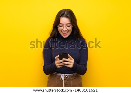 Teenager girl over isolated yellow wall sending a message with the mobile
