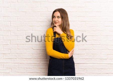 Teenager girl over white brick wall thinking an idea while looking up