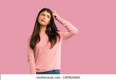 Teenager girl with pink shirt having doubts while scratching head on isolated pink background
