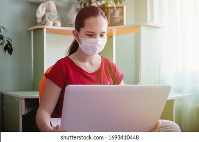 Teenager Girl With Protective Mask Studying Online At Home With A Laptop During The Coronavirus Epidemic. Home Schooling. Social Distancing. Online School.