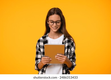 Teenager girl schoolchild pupil student using digital tablet for e-learning, surfing web pages social media, blogging, vlogging, shopping online isolated in yellow background - Powered by Shutterstock