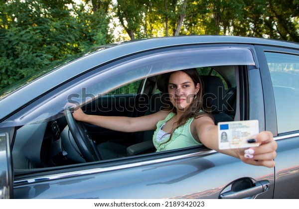 Teenager\
girl  showing his driver\'s license in the car window after passing\
the exam or at the request of the traffic\
police