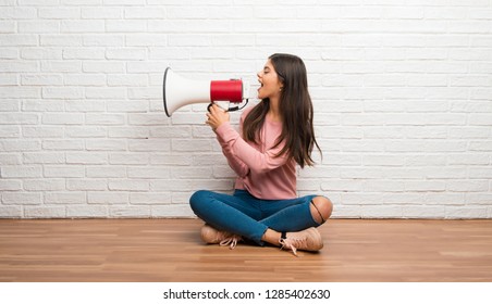 Teenager Girl Sitting On The Floor In A Room Shouting Through A Megaphone To Announce Something In Lateral Position