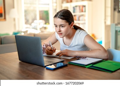 Teenager girl studying online at home looking at laptop at  quarantine isolation period during pandemic. Home schooling. Social distancing. Online school test.