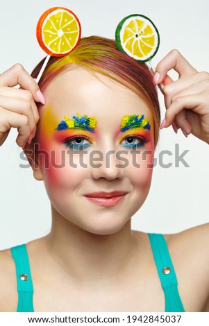Teenager girl with unusual face art make-up . Child with lollipops in hands on head like ears. Sweet tooth concept.