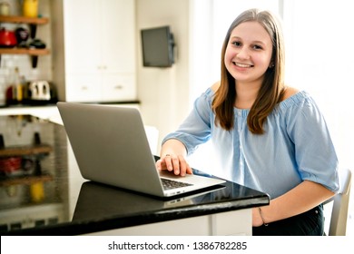 teenager girl using laptop studying in kitchen