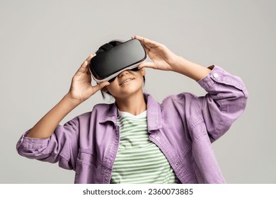 Teenager girl in virtual glasses goggles watching movie playing video games on gray background. Smiling teen enjoying virtual world in VR helmet. Cyberspace, entertainment, online recreation concept. - Powered by Shutterstock