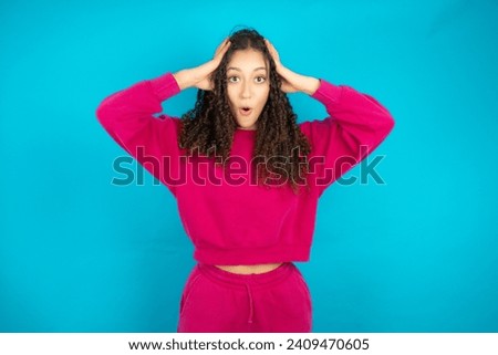 teenager girl wearing pink jumper  with scared expression, keeps hands on head, jaw dropped, has terrific expression. Omg concept