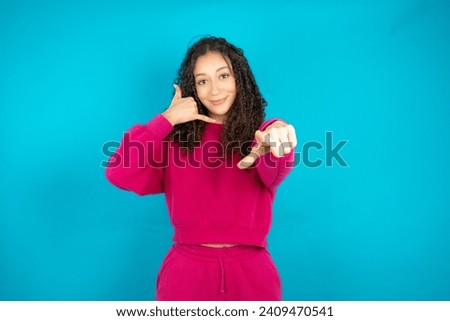 teenager girl wearing red knitted jumper smiling cheerfully and pointing to camera while making a call you later gesture, talking on phone