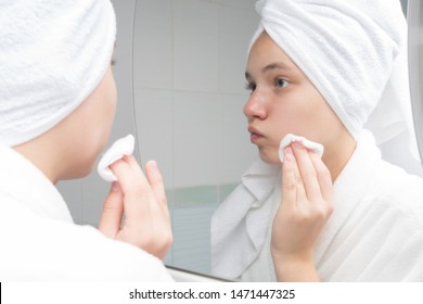 teenager girl wipes her face with acne in the morning, standing in front of a mirror