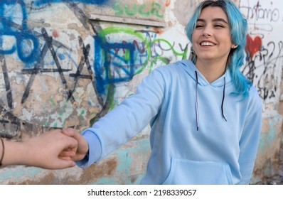 Teenager Girls Holding Hands And Laughing. Blue Haired Young Woman Wearing Hoodie Spending Time With Friends Outdoor Near Graffiti Wall. Clothing Mockup.