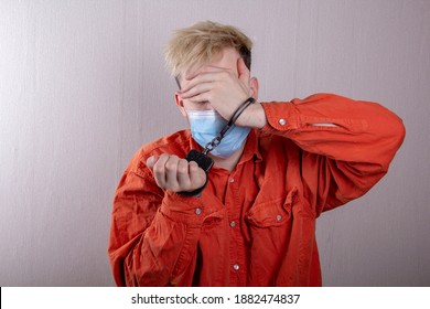 A Teenager In Handcuffs And A Medical Mask Holds His Head Against A Gray Background.Headache For Juvenile Delinquents In Quarantine, Criminal Liability. Members Of Youth Criminal Groups.