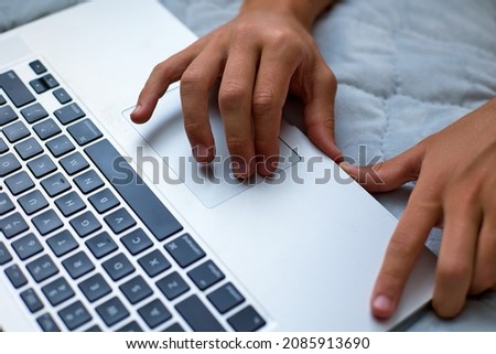 Teenager hands working on the laptop lying down at home. Concept of convenient use of a touchpad instead of a computer mouse on a modern laptop