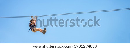 Teenager having fun on a zipline on panoramic blue sky background with copy space.