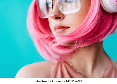 A Teenager In Headphones And Glasses With Pink Hair. Bright Extravagant Appearance. Modern Youth Culture. Portrait Of A Girl With A Short Haircut On A Blue Background. Mockup Friendly. 