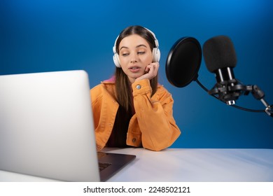 Teenager in headphones looking at laptop while recording podcast isolated on blue - Powered by Shutterstock