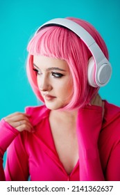 A Teenager In Headphones With Pink Hair. Bright Extravagant Appearance. Modern Youth Culture. Portrait Of A Girl With A Short Haircut On A Blue Background. Mockup Friendly. 