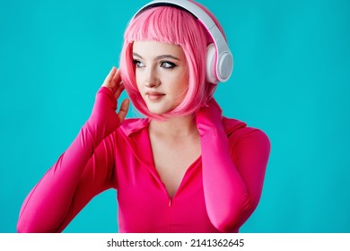 A Teenager In Headphones With Pink Hair Takes. Bright Extravagant Appearance. Modern Youth Culture. Portrait Of A Girl With A Short Haircut On A Blue Background. Mockup Friendly. 