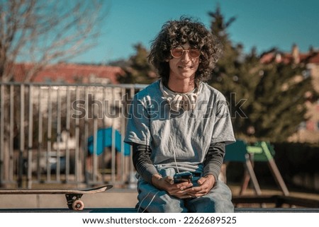 teenager with headphones and with skateboard sitting in skate park