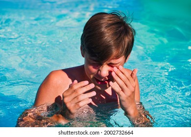 The teenager hides his face with his hands in the pool, wiping water from his eyes while swimming in the pool. Eye irritation from chlorinated water