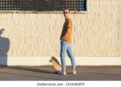 Teenager With His Back Turned Looking At The Camera With Sunglasses Enjoying His Surf Board And Costal Life