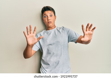 Teenager hispanic boy wearing casual grey t shirt afraid and terrified with fear expression stop gesture with hands, shouting in shock. panic concept.  - Powered by Shutterstock