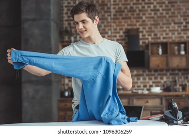 Teenager Holding Blue Shirt Near Ironing Board With Iron