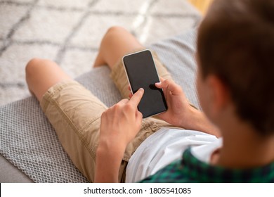 Teenager holding mobile phone with empty screen, sitting on sofa at home, top view, closeup - Shutterstock ID 1805541085