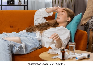 Teenager ill red hair girl suffering from cold or allergy lying on sofa couch in living room at home. Sick child blows sneezes wipes snot into napkin. Coronavirus quarantine, pandemic, flu. Lifestyles - Powered by Shutterstock