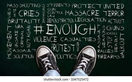 A Teenager In Jeans And Canvas Shoes Standing On Chalkboard With # ENOUGH Word Cloud. Concept Of Social Movement To Protest Gun Violence And Mass School Shootings In The United States.