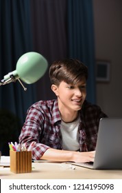 Teenager With Laptop Doing Homework At Table In Evening