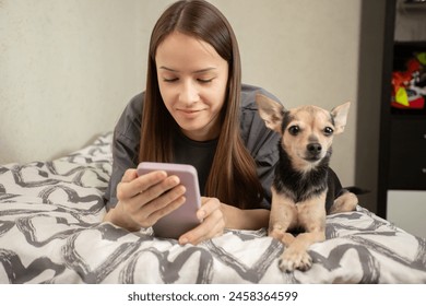 Teenager lying on bed with phone and dog, watching videos together, pet and owner immersed in entertainment, enjoying a cozy evening at home. - Powered by Shutterstock