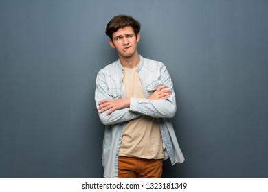 Teenager Man With Jean Jacket Over Grey Wall With Confuse Face Expression While Bites Lip