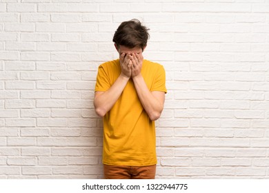 Teenager man over white brick wall with tired and sick expression