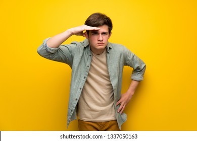 Teenager man over yellow wall looking far away with hand to look something