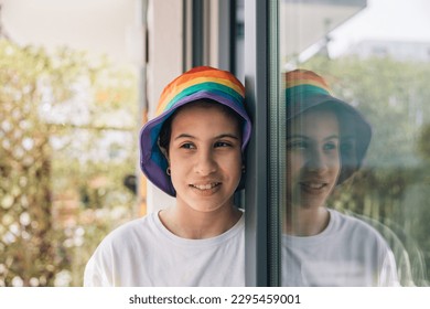 Teenager with rainbow hat smiling reflected in window, LGBTQ+ Pride Month concept - Powered by Shutterstock