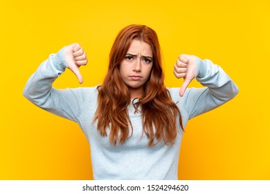 Teenager Redhead Girl Over Isolated Yellow Background Showing Thumb Down